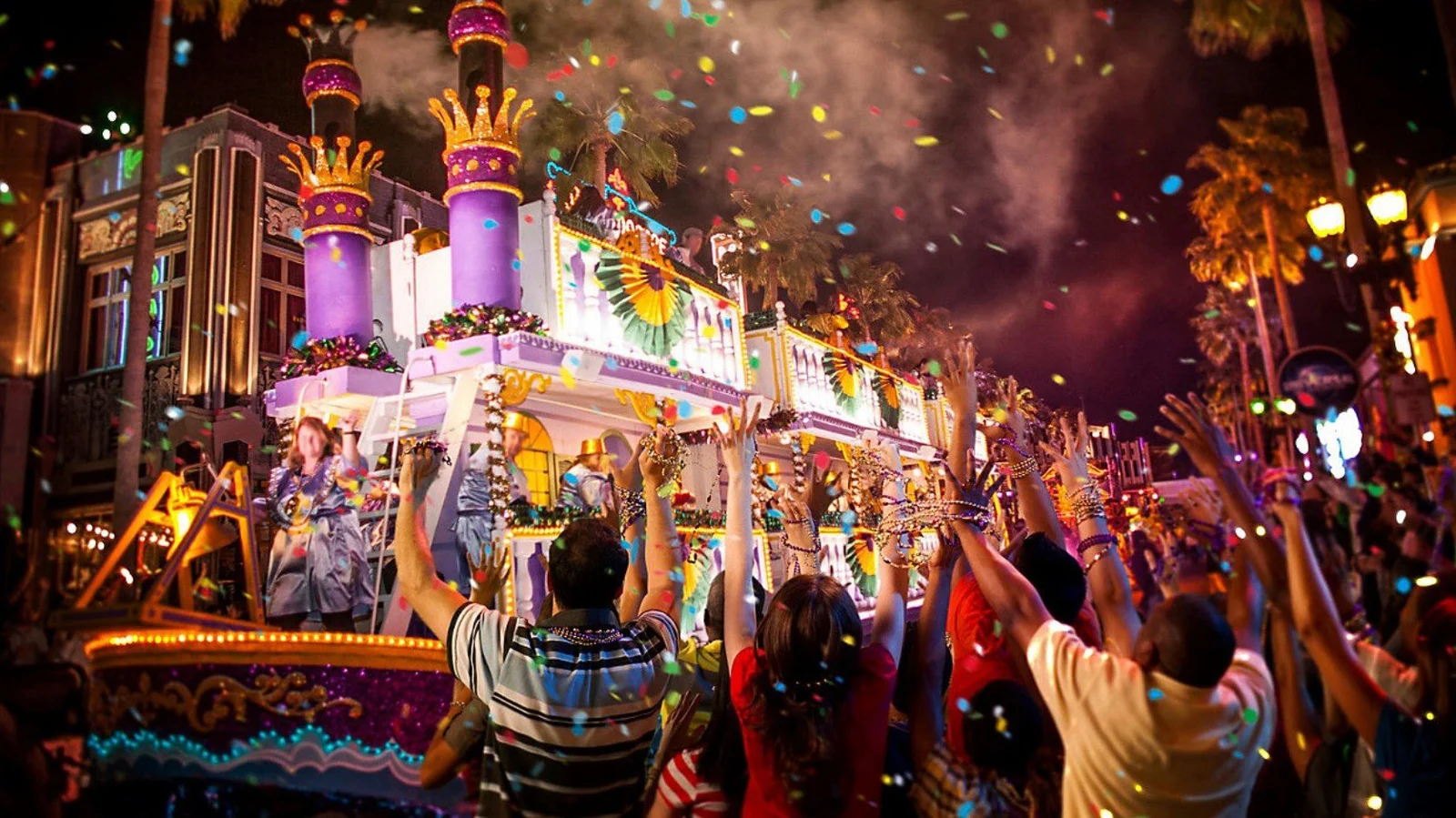 Universal Orlando Mardi Gras parade with colorful floats, confetti, and crowds reaching for beads at night