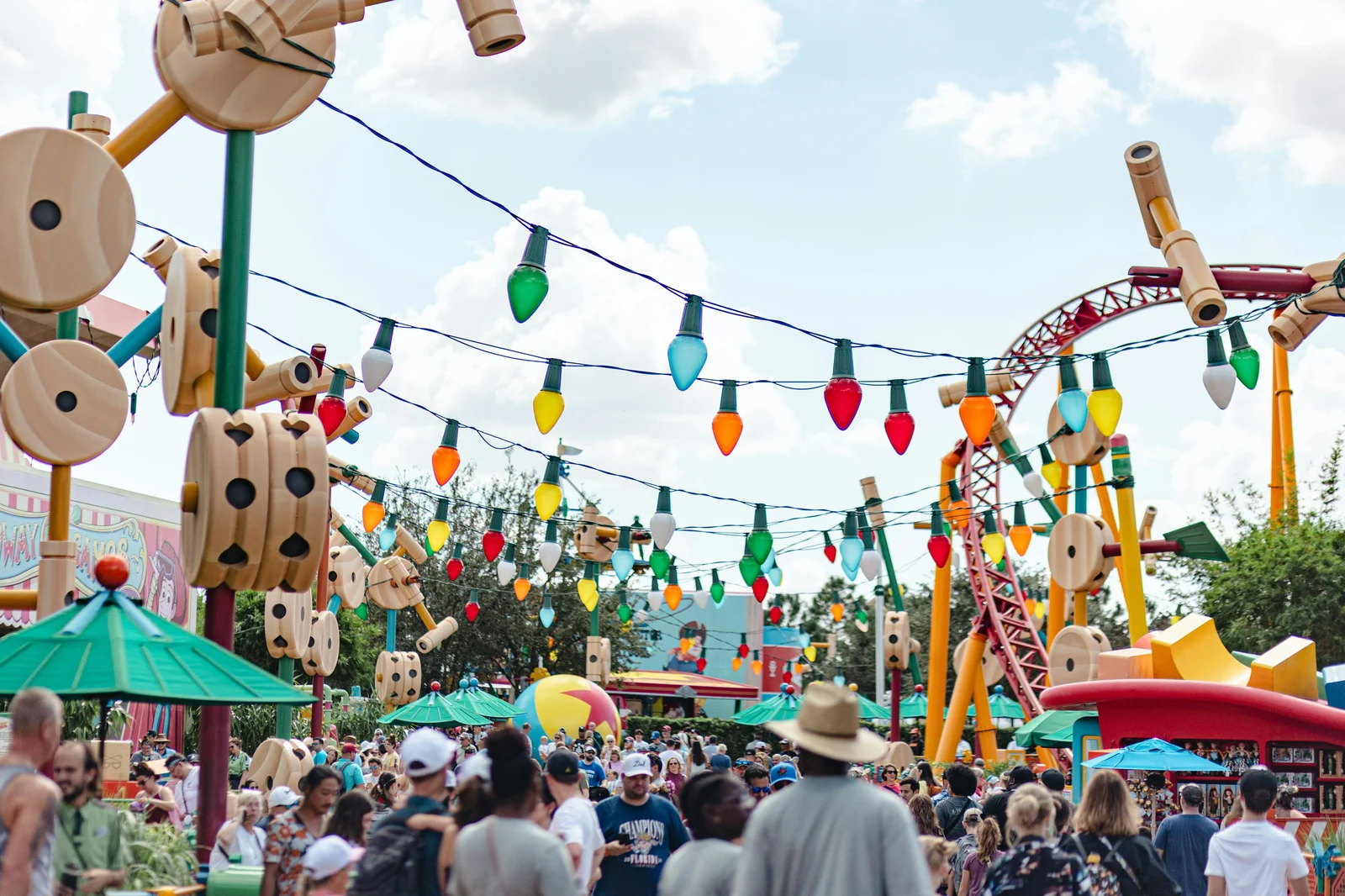 Colorful theme park area with hanging lights, roller coaster, and summer crowds in Orlando